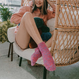 Person sitting on a wicker chair wearing colorful, fuzzy pink socks. thumbnail