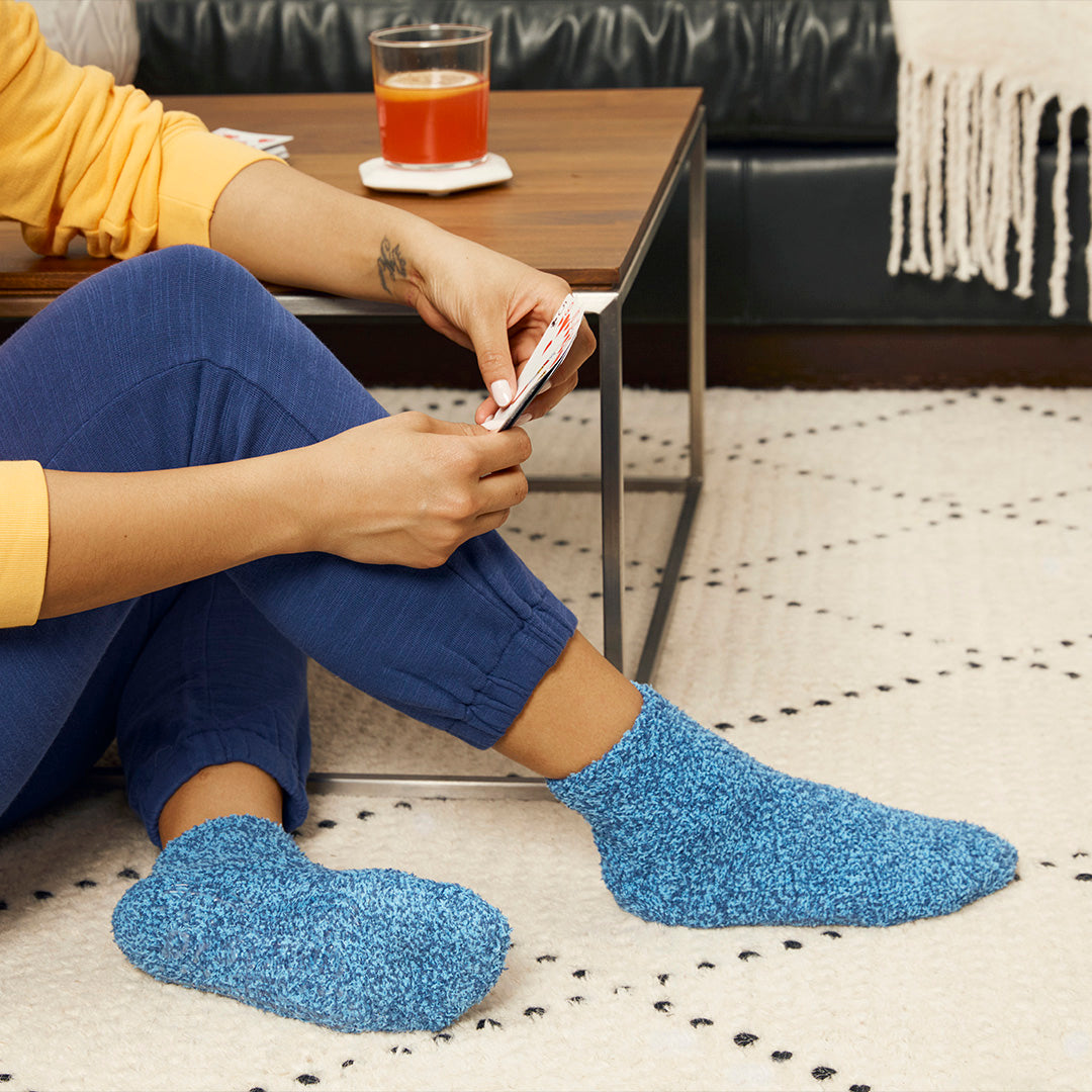 Person wearing blue socks sitting on a patterned rug with a glass of juice on a table.