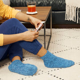 Person wearing blue socks sitting on a patterned rug with a glass of juice on a table.