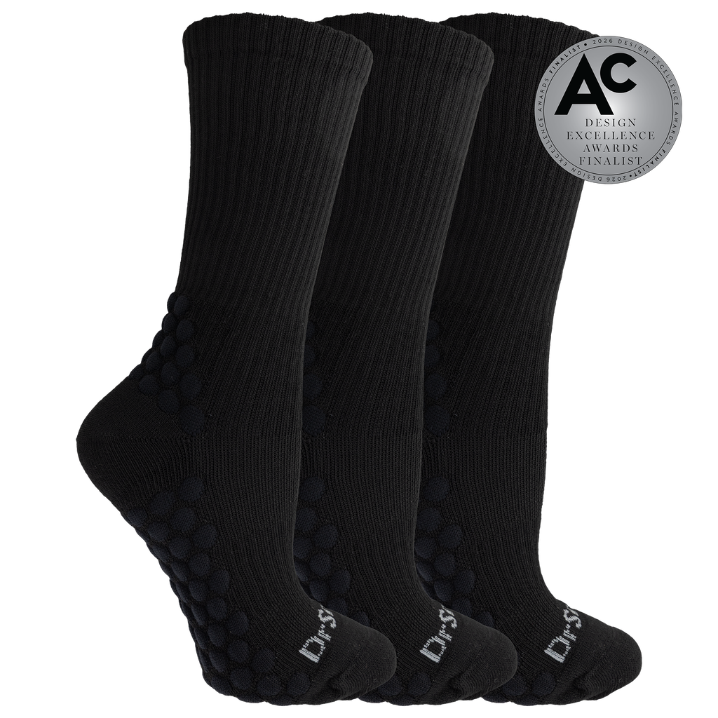 Three black crew socks with textured grip dots on the sole and heel, shown on a white background with a silver award badge overlay.