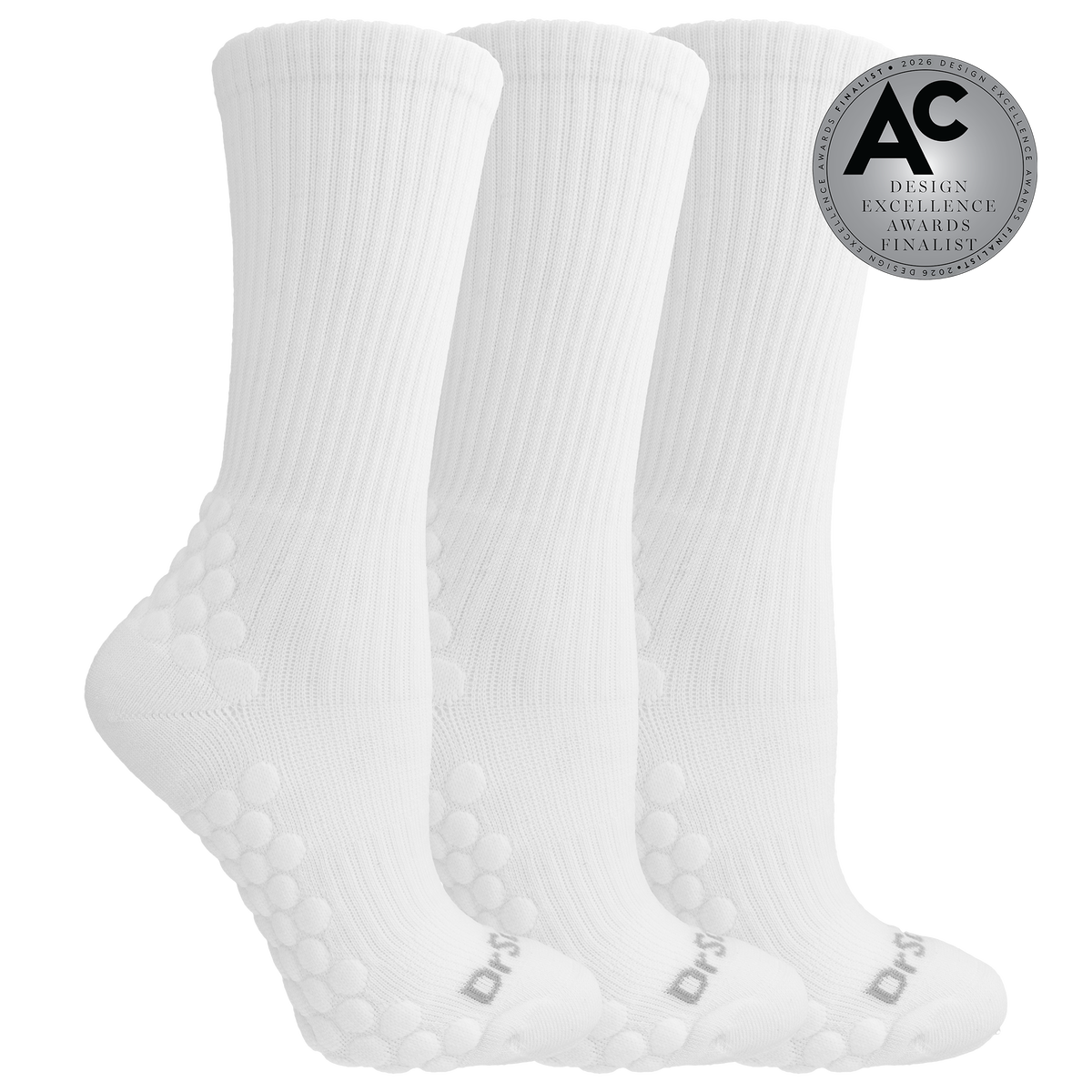 Three white ribbed crew socks with raised grip dots on the sole and heel, shown on a white background with a silver award badge reading Design Excellence Awards 2026 Design Finalist.
