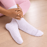 White ribbed ankle socks with textured grip dots on the sole, worn by a person sitting on a light wood floor. thumbnail