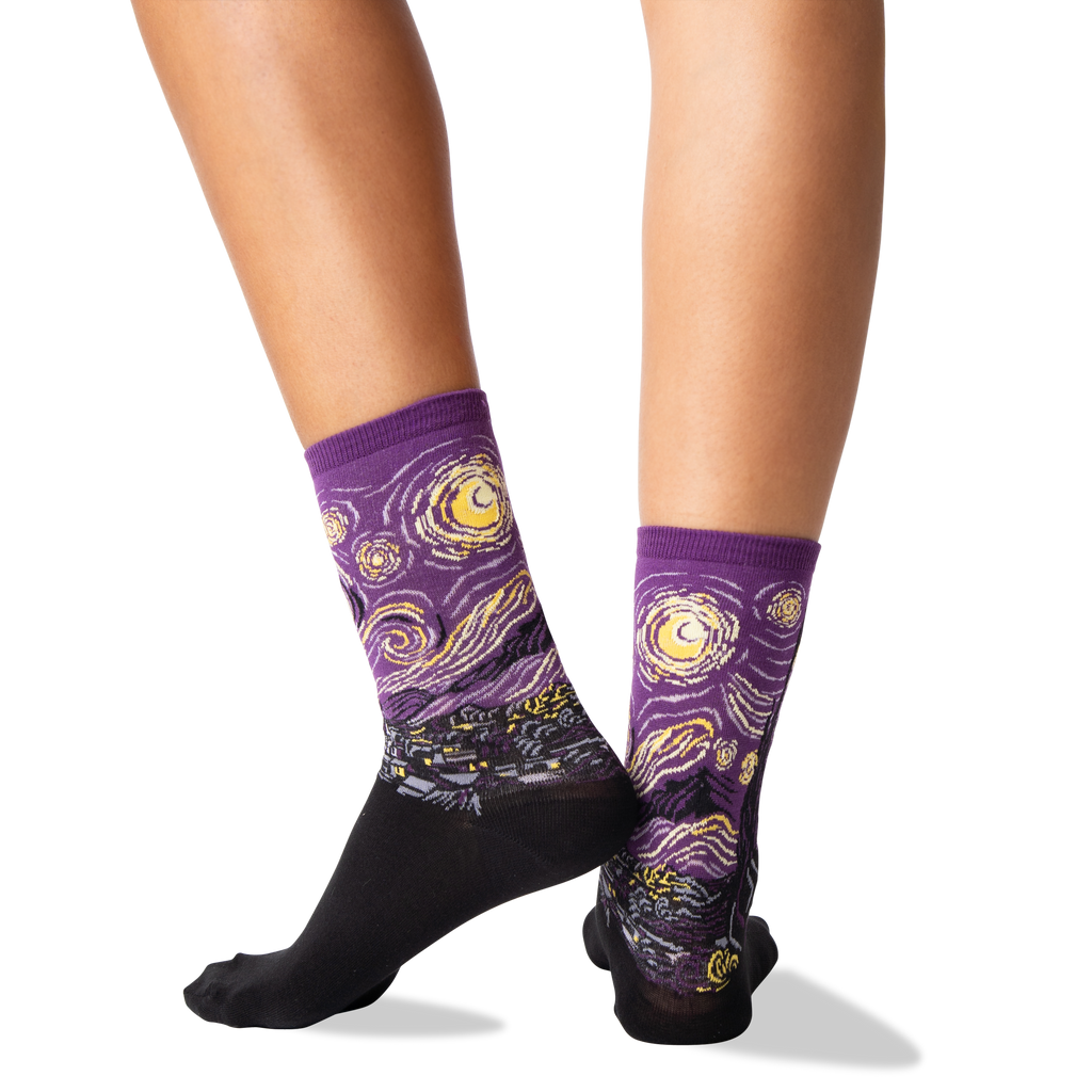 A person's legs wearing crew socks with a Van Gogh-inspired swirling night sky pattern in purple, yellow, and white, with black soles, shown against a plain white background.