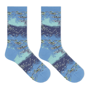 A pair of crew socks with a detailed watercolor-style print of a lake or river scene, featuring blue and light teal water, white ripples, and green reeds, displayed against a solid white background.
