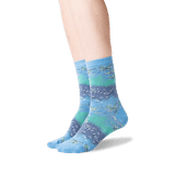 A pair of crew socks with a horizontal striped pattern in shades of blue, teal, and purple, featuring a fish design, shown on a model's feet against a white background.