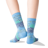 A pair of crew socks worn on feet, featuring an abstract landscape-like print in shades of light blue, teal, and lavender-gray with white and gray brushstroke details. The background is a clean white studio backdrop. thumbnail