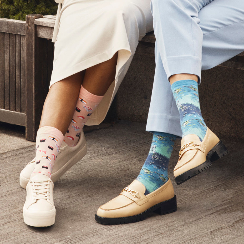 Two women sitting on a bench wearing HOTSOX novelty socks.