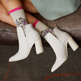 A person seated on a brown leather bench wearing off-white ankle boots with block heels and patterned socks featuring a pink cuff.