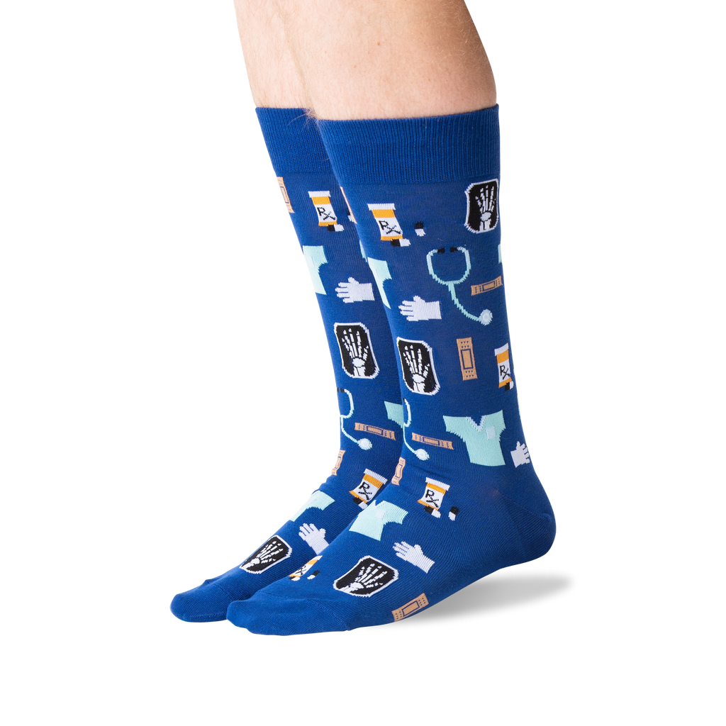 A pair of crew socks worn on lower legs, featuring a medical-themed print with X-rays, stethoscopes, pills, and medical icons on a royal blue background.