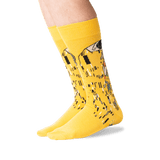 A pair of bright yellow crew socks with a stylized piano-key and figure graphic in black, white, and gray, worn on a person's feet against a clean white background. thumbnail