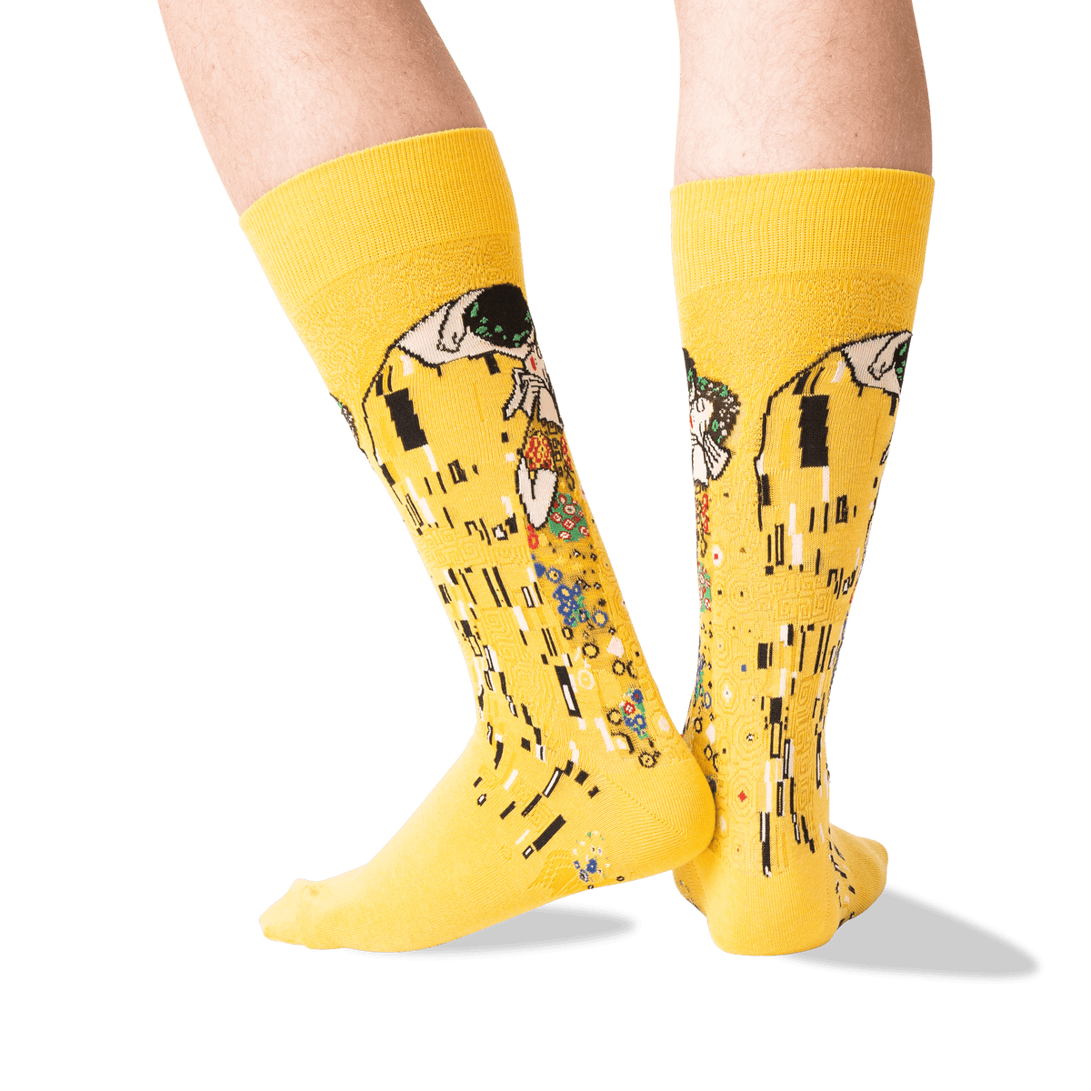 A pair of bright yellow crew socks with a Gustav Klimt-style art print featuring black, white, green, and orange details, shown on a person's legs against a clean white background.