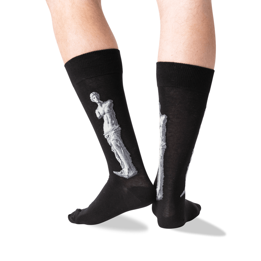 A pair of black crew socks worn on a person's legs, featuring a large white sculpture design on the side of each sock, photographed against a clean white background.