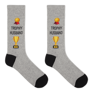 A pair of heather gray crew socks with black heels and toes, featuring a gold trophy graphic and the text 'TROPHY HUSBAND' printed on the front.