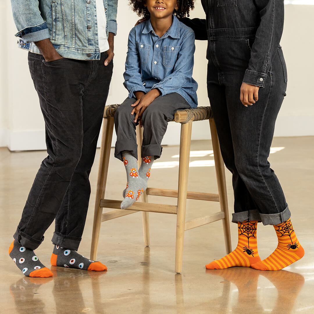Child sitting on a stool with two adults wearing colorful socks in a casual setting.
