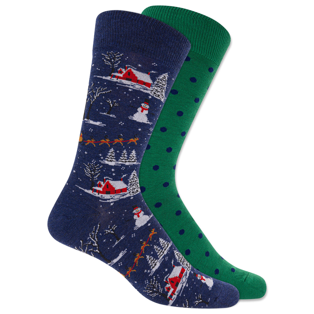 A pair of crew socks shown overlapping on a white background. The front sock is navy blue with a winter village pattern featuring red cabins, snow, trees, and orange sleighs.