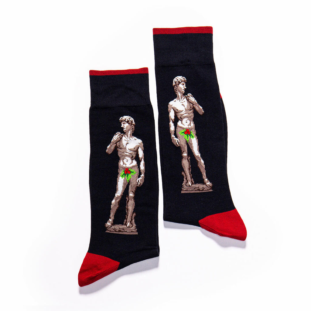 A pair of black crew socks with red cuffs, heels, and toes, featuring a graphic print of Michelangelo's David statue with a green bow-tie overlay.