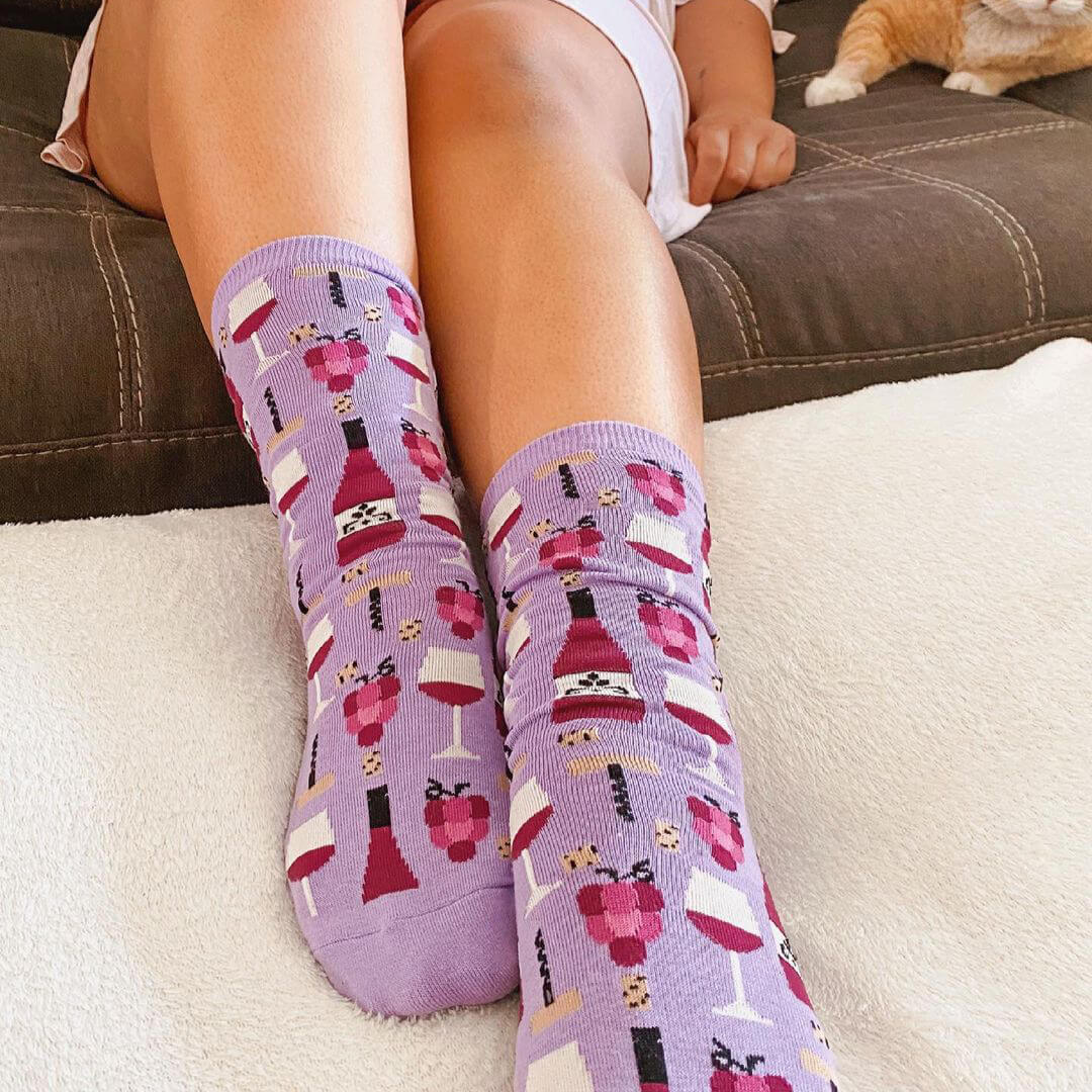 Purple socks with wine-themed pattern worn by a person sitting on a couch.