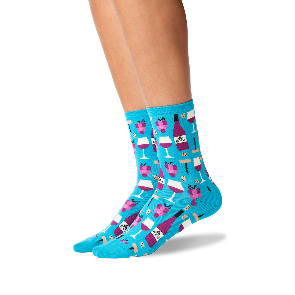 A pair of bright turquoise crew socks with a repeating pattern of pink champagne bottles, glasses, and champagne bubbles, shown on a person's feet against a white background.