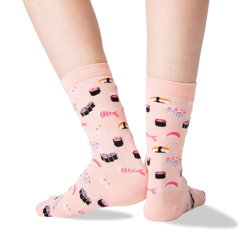 A pair of light pink crew socks with a sushi print, shown on a person's feet against a clean white background.