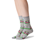 A pair of gray crew socks with a colorful golf course and golf cart pattern, worn on a person's feet against a white background.