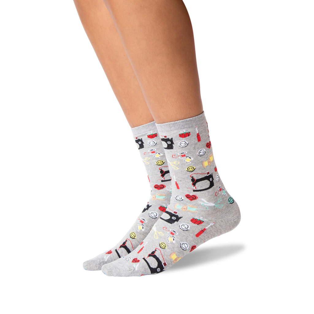 A pair of light gray crew socks with a colorful cartoon pattern of sewing machines, shown on a model's feet against a white background.