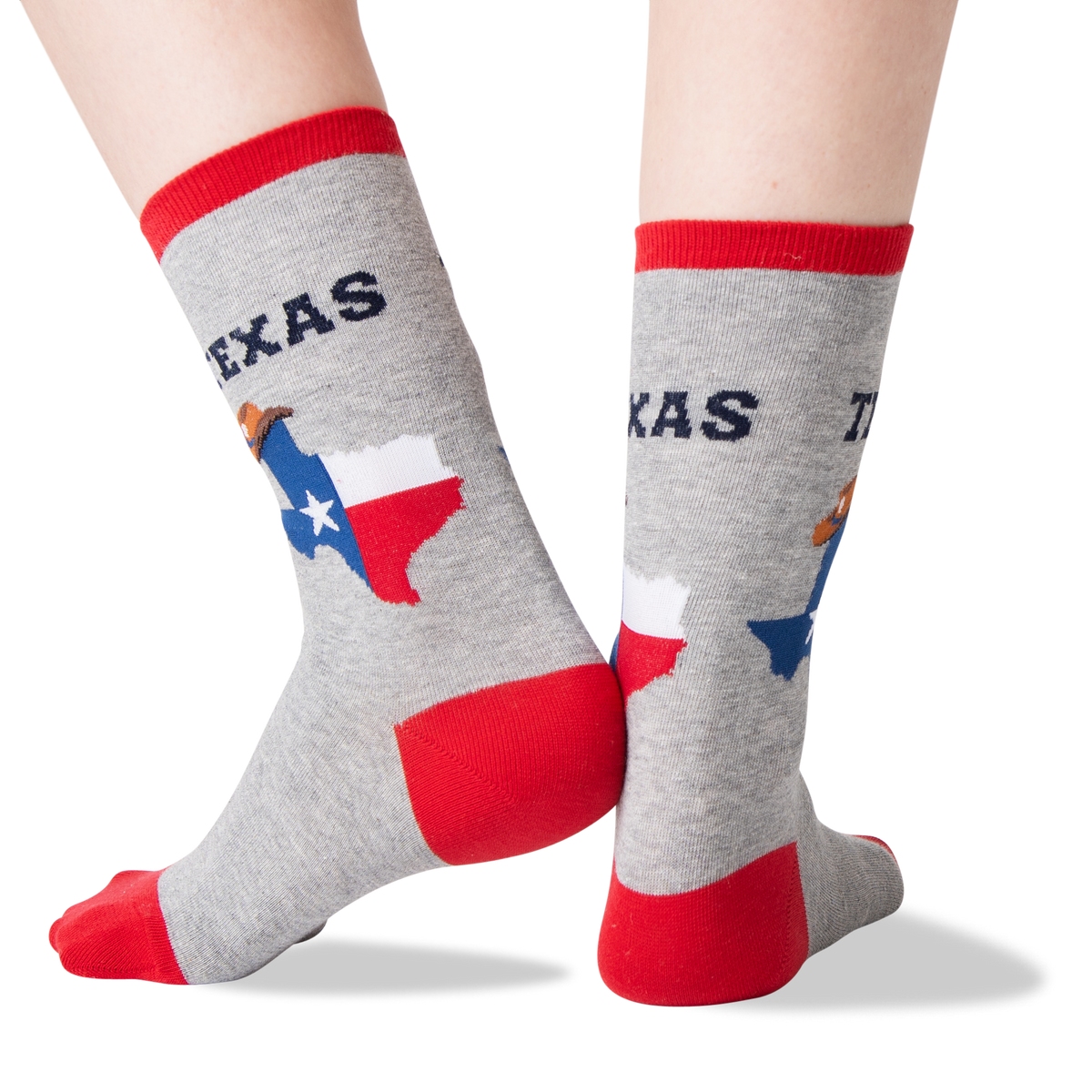 A pair of crew socks worn on feet, shown against a plain white background. The socks are heather gray with red cuffs, heels, and toes, and feature a graphic of the state of Texas with the word 'TEXAS' above it.