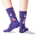A pair of purple crew socks with a repeating pattern of dogs dressed in Halloween costumes, shown on a person's feet against a clean white background.