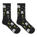 A pair of black crew socks with a Halloween-themed print featuring green zombie hands, gray tombstones, and gray bats, displayed against a solid white background.