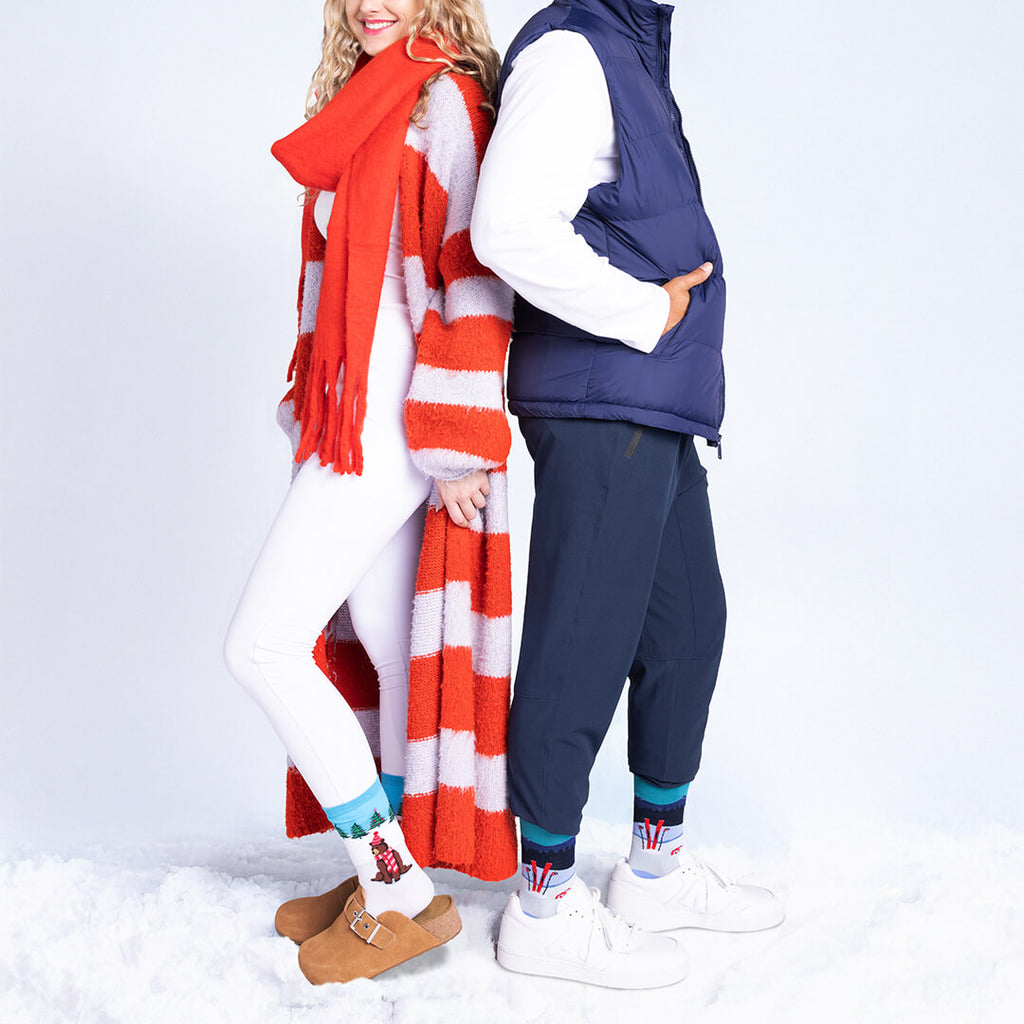 Two people standing in the snow wearing winter clothing with a red scarf and blue vest.