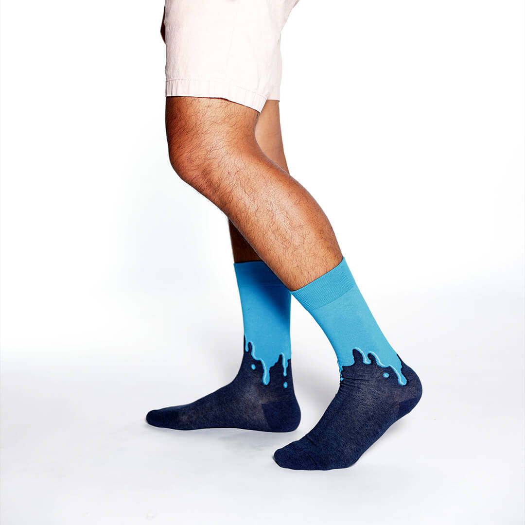 A person's legs wearing crew socks with a dark navy blue base and a bright blue dripping design along the top, shown against a plain white studio background.