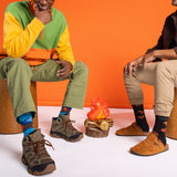 Two people sitting on stools with colorful socks and shoes, wearing patterned socks. thumbnail