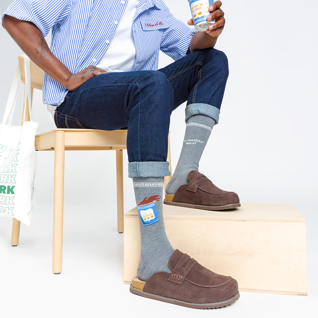 Person wearing gray socks with brand labels, sitting on a chair holding a can.