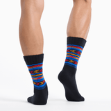 A pair of crew socks worn on a model's legs, featuring a black base with vibrant horizontal stripes in blue, red, orange, and yellow on the upper portion. thumbnail