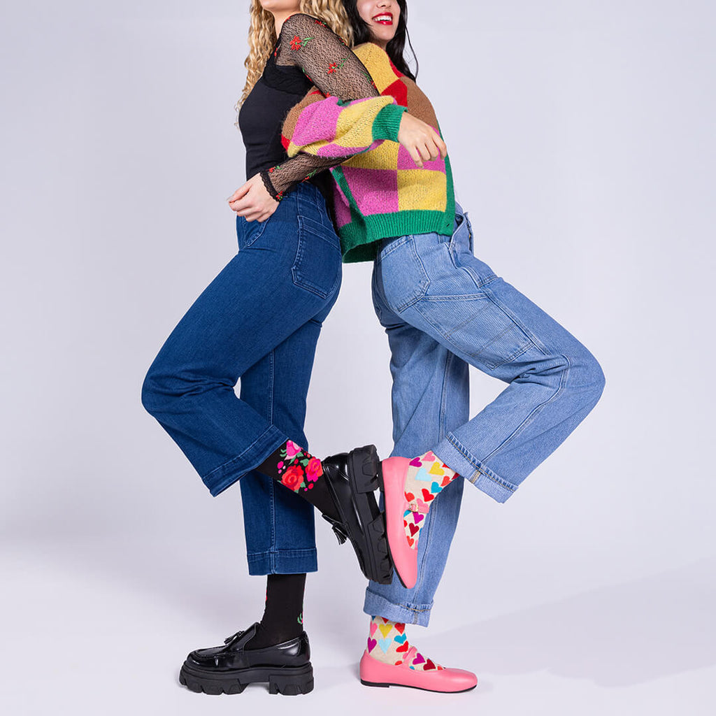 Two people hugging, one wearing a colorful sweater and jeans, the other in black top and blue jeans, on a white background.