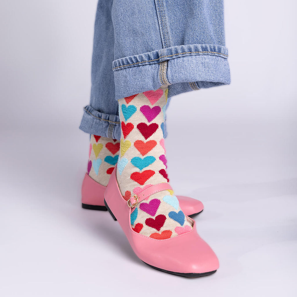 Colorful heart-patterned socks worn with pink shoes and blue jeans on a light gray background