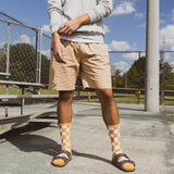 Person wearing beige shorts and checkered socks standing on a concrete surface with a chain-link fence and trees in the background.