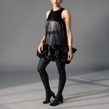 Woman wearing a black dress with ruffled layers and tights on a gray background thumbnail