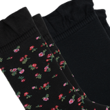 Two black socks arranged diagonally on a white background, with two featuring a small pink and red floral pattern with green leaves and one solid black sock.