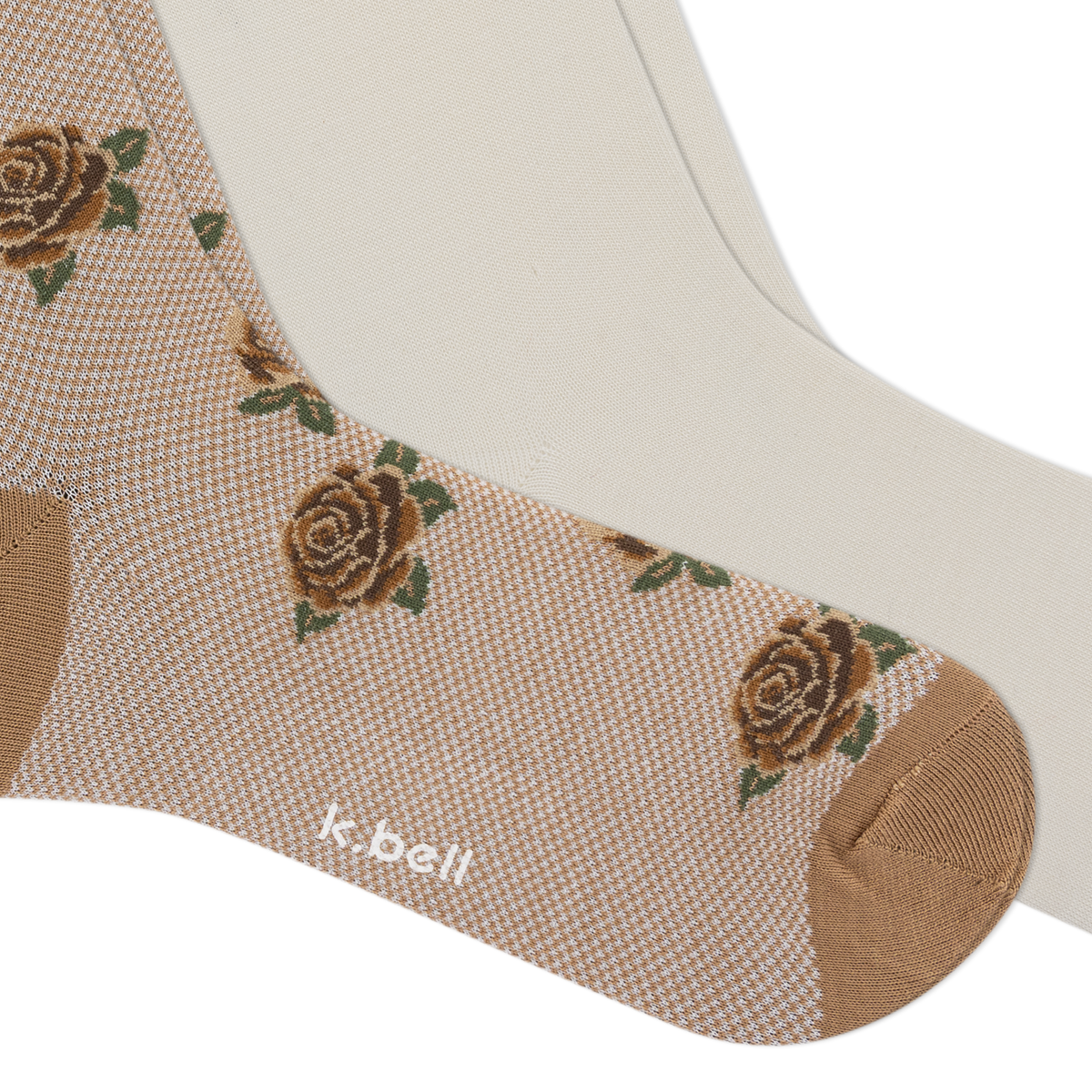 A close-up of a beige sock with a woven rose pattern, brown toe and heel, another pair of light cream socks, and the brand name 'k.bell' printed near the ankle.