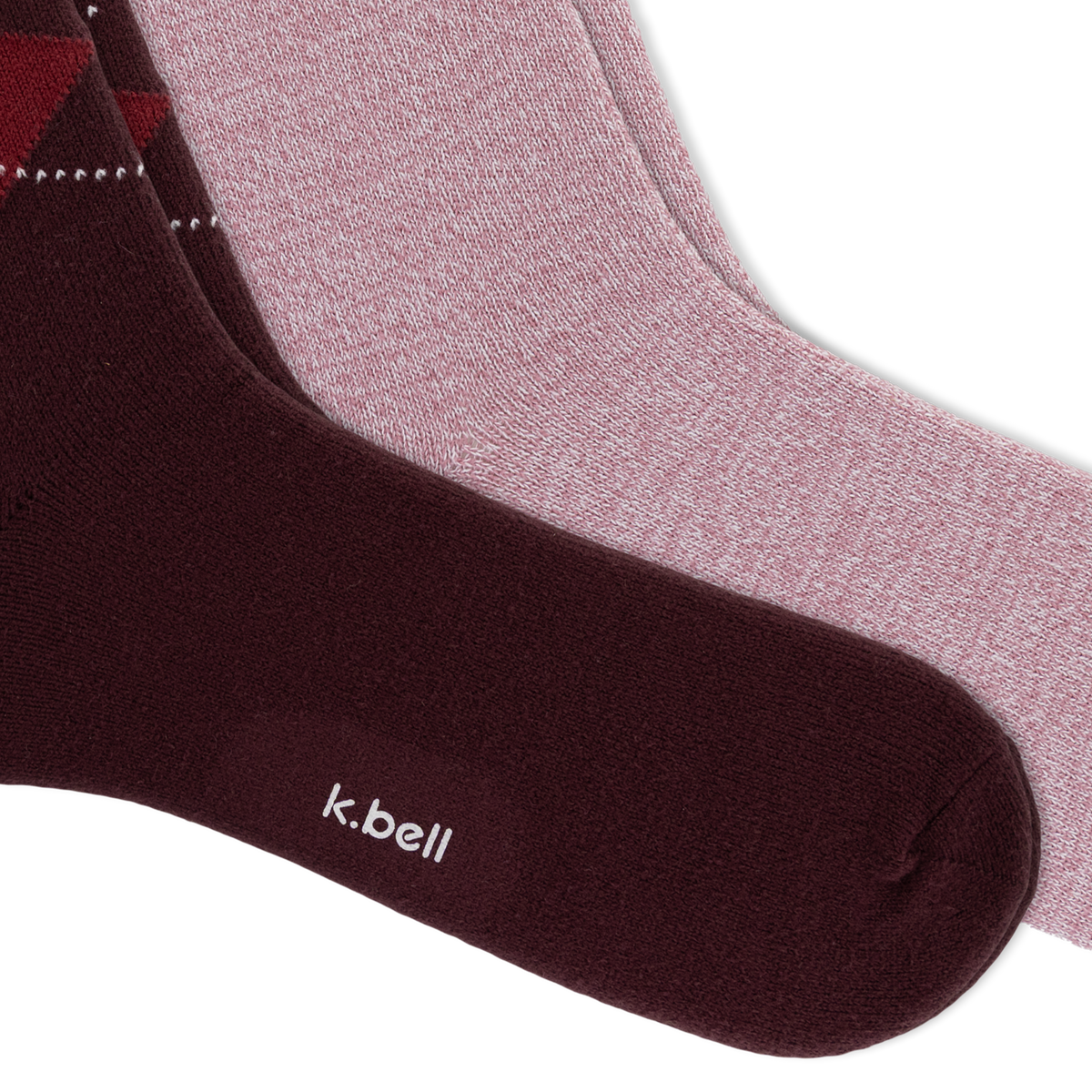 Two pairs of crew socks from k.bell, featuring a dusty rose pair, and a red and navy argyle pattern on a dark burgundy pair, arranged diagonally on a white background.