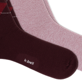 Two pairs of crew socks from k.bell, featuring a dusty rose pair, and a red and navy argyle pattern on a dark burgundy pair, arranged diagonally on a white background. thumbnail
