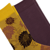 Two folded dress socks shown on a white background. One sock is gold with a dark brown and mauve floral pattern, and the other is solid deep plum purple.