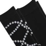 Two pairs of black dress socks stacked diagonally, featuring a textured knit pattern with a silver glittery geometric diamond design on the lower half.