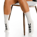 White socks with 'Iconic' branding worn by a person sitting on a chair.