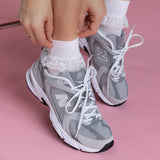 Person wearing gray sneakers with white laced ankle socks on a pink background