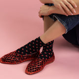 Person wearing red mesh shoes and black socks with red patterns on a pink background thumbnail