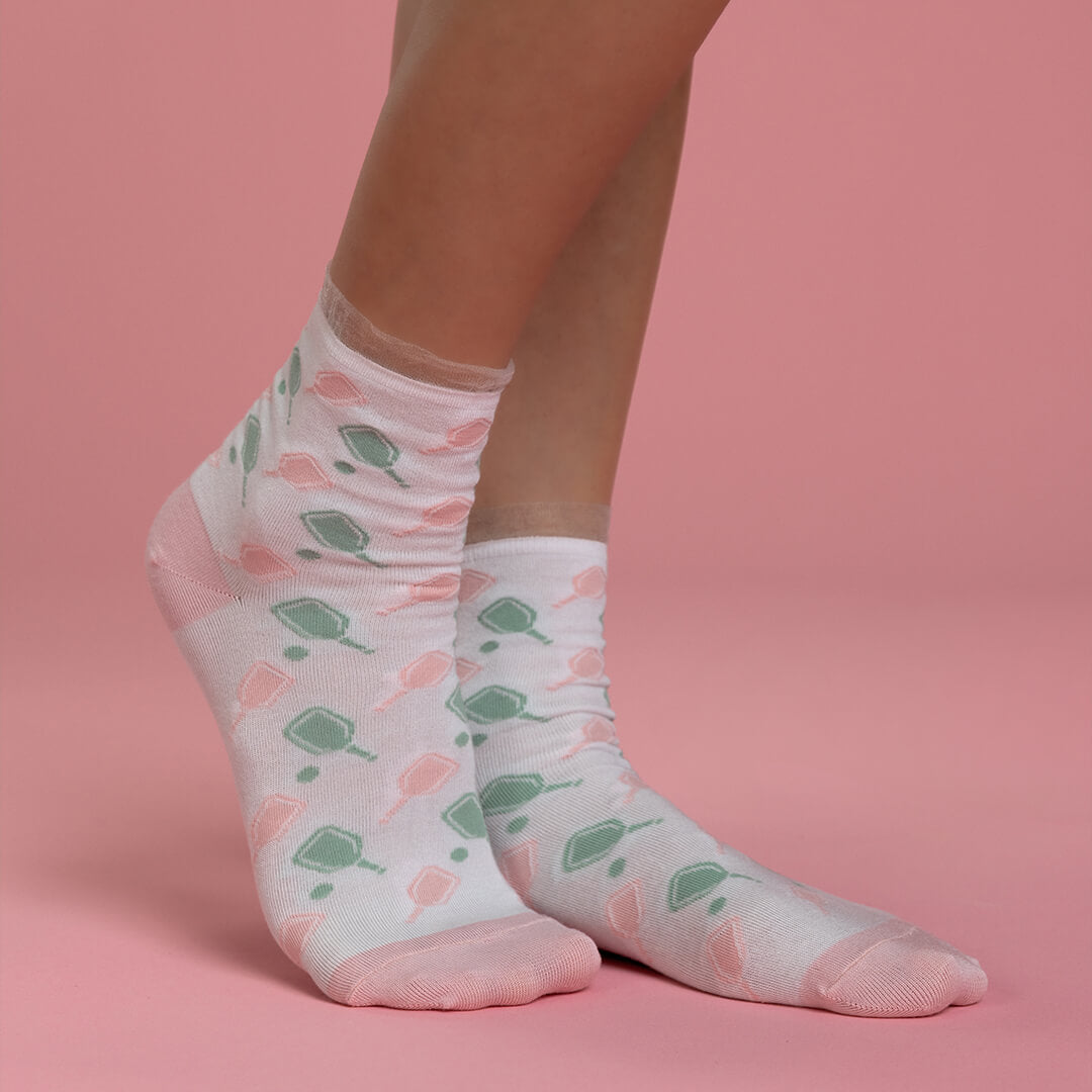 White socks with green and pink pickleball patterns worn by a person on a pink background