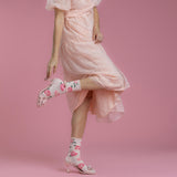Woman wearing a pink dress and floral high-heeled shoes on a pink background