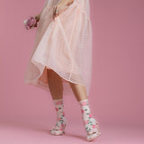 Person wearing a light pink dress and floral socks on a pink background