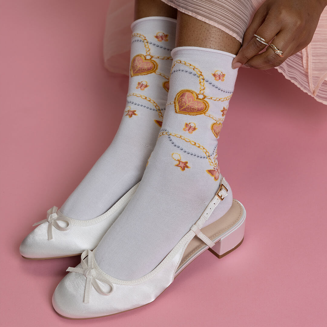 White socks with heart and chain design worn with white shoes on a pink background